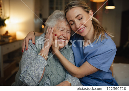 Caring healthcare worker visiting a senior patient at home, hugging her. 122560728