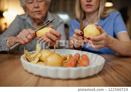 Portrait of elderly companion assistant and senior woman peeling potatoes. Home health care services. Portrait of elderly companion assistant and senior woman peeling potatoes. Home health care services. 122560729