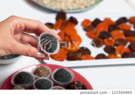 Woman puts dried fruit candies on a plate. Balls of prunes, dates and coconut. With a sprinkle of black sesame powder. 122560969