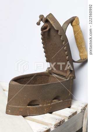 Old iron, heated by hot coals. Opened coal compartment. Located on the a wooden box. 122560992