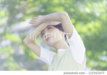 A middle-aged woman holds her hand up to block the sunlight amidst fresh greenery 122561077