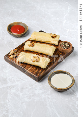 Crepes filled with mushrooms and cheese on a wooden platter 122561174