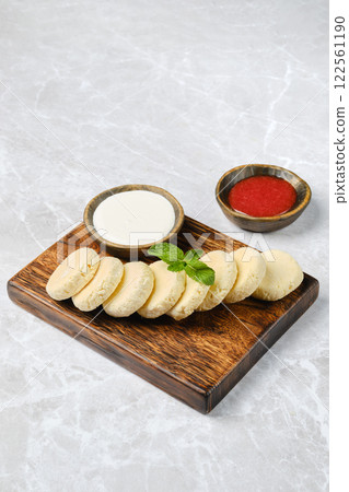 A wooden platter displays a stack of soft curd patties accompanied by bowls of sour cream and strawberry jam A wooden platter displays a stack of soft curd patties accompanied by bowls of sour cream and strawberry jam 122561190