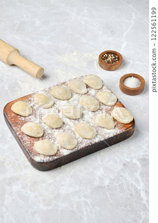 Freshly made dumplings ready for cooking on a wooden board with a rolling pin 122561199