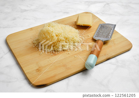 Shredded cheese on wooden cutting board with grater and cheese block 122561205