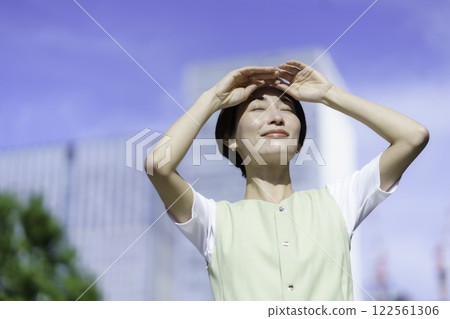 一位中年婦女在翠綠的樹林中舉起手遮擋陽光 一位中年婦女在翠綠的樹林中舉起手遮擋陽光 122561306