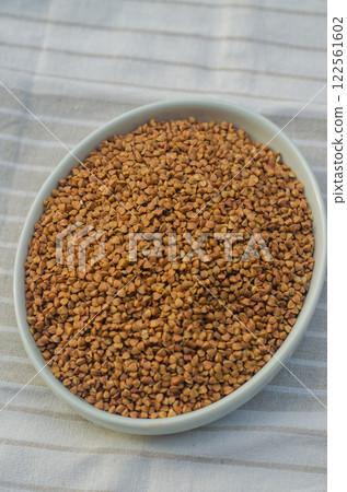 Bowl filled with raw buckwheat grains on a striped fabric background. High quality photo 122561602