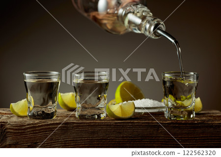 Tequila with salt and lime slices on a old wooden board. Tequila with salt and lime slices on a old wooden board. 122562320