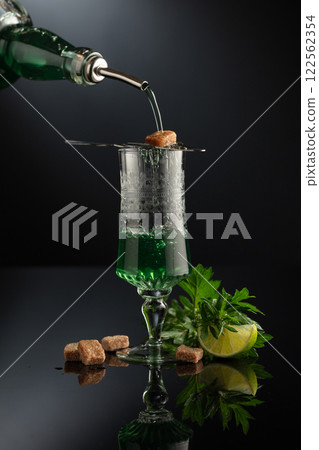 Absinthe is poured from an vintage bottle into a glass. 122562354