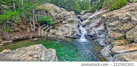 Scenic waterfall flowing into a green natural pool surrounded by rocky forest landscape Scenic waterfall flowing into a green natural pool surrounded by rocky forest landscape 122562383
