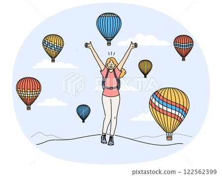 Woman traveler stands among rising balloons and joyfully raises hands up enjoying trip to festival 122562399