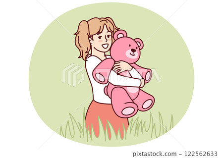 Happy little girl with teddy bear in hands stands in meadow among tall grass and looks at screen 122562633