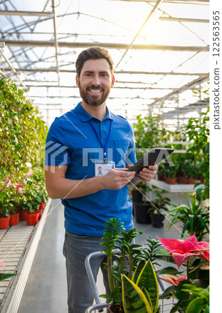 Cheerful man worker in floral industry arranging flowers for sale in greenhouse 122563565