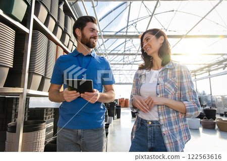 Salesman in retail store showing many pots for plants on shelves to female customer 122563616