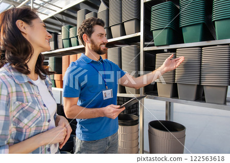 Salesman in retail store showing many pots for plants on shelves to female customer 122563618