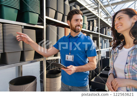 Bearded man worker assisting woman customer with purchasing products for flowers cultivating in retail market 122563621