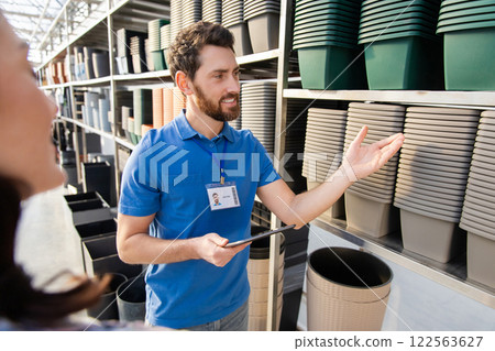 Salesman in retail store showing many pots for plants on shelves to female customer Salesman in retail store showing many pots for plants on shelves to female customer 122563627