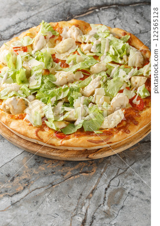 Caesar pizza with white sauce, cheese, tomatoes, chicken breast and lettuce close-up on a wooden board. Vertical 122565128