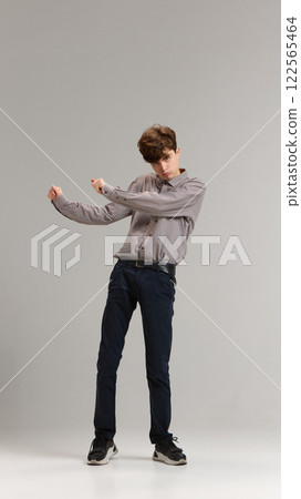Full-length of teen boy, student in shirt and jeans emotionally dancing in excitement against grey studio background Full-length of teen boy, student in shirt and jeans emotionally dancing in excitement against grey studio background 122565464