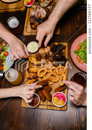 A top-down view of hands reaching for assorted appetizers on a wooden platter. 122566157