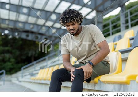A man injured his leg while doing active physical exercises and fitness, a sportsman massages his knee muscle while sitting. 122566252