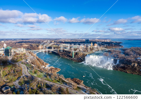 Niagara Falls City, Ontario, Canada - December 19 2021 : Overlooking the Niagara River Rainbow Bridge and American Falls in a sunny day. 122566600