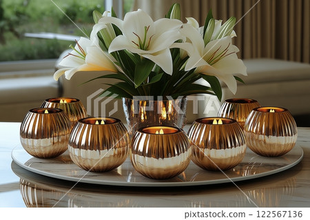 Shiny rose-gold spherical candle holders on a reflective tray, paired with blooming lilies and soft light 122567136