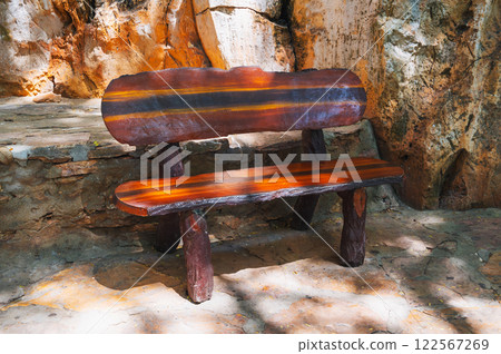 Front view of a park bench made of dark brown wood on the stone pavement of the park complex. Front view of a park bench made of dark brown wood on the stone pavement of the park complex. 122567269