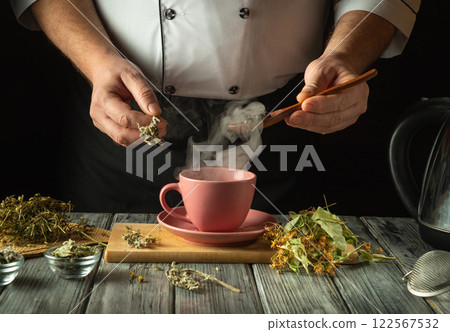 An experienced herbalist brews a healthy tea from medicinal dry herbs. A hand holds a spoon with dry rose hips to be added to a pink cup. Traditional medicine concept 122567532