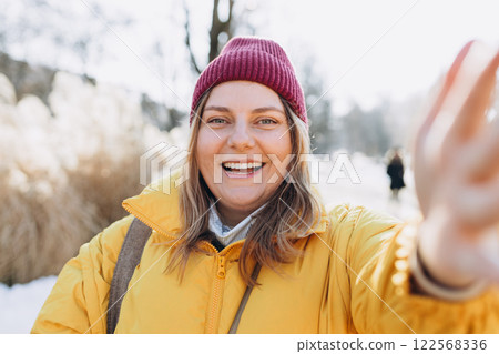 Smiling woman in winter clothing taking photo on park background. Selfie time. Holidays, rest, blogging banner. Charming female wearing stylish outfit have fine 122568336