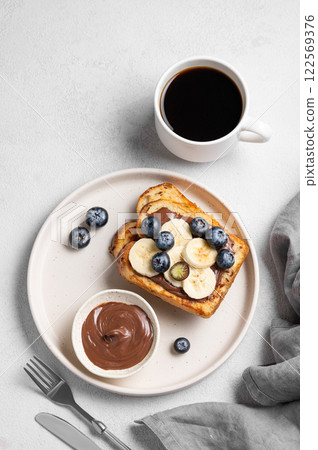 Toasted bread with chocolate cream, blueberries and banana on a plate on a light background 122569376
