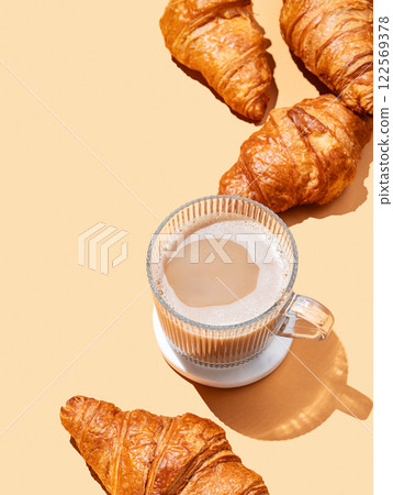 Fresh croissants and cup of cappuccino coffee or latte on orange background with shadow. 122569378