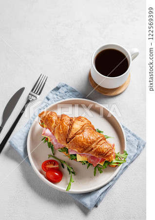 Croissant sandwich with ham, cheese, tomato  and arugula on a plate on a light background  122569399