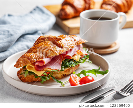 Croissant sandwich with ham, cheese, tomato and arugula on a plate on a white background Croissant sandwich with ham, cheese, tomato and arugula on a plate on a white background 122569400