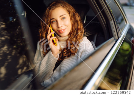 Positive young woman in casual clothes sits in the back seat of a car with a mobile phone. Positive young woman in casual clothes sits in the back seat of a car with a mobile phone. 122569542