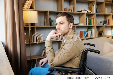 A young handsome man in a wheelchair looks out the window with a sad look 122569776