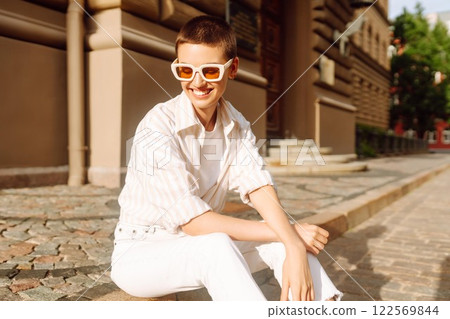 Hipster fashion woman in stylish glasses sits on a curb in the street in Europe. Hipster fashion woman in stylish glasses sits on a curb in the street in Europe. 122569844