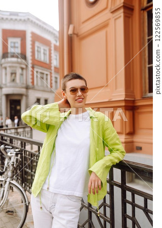 Positive woman with a short haircut and a green shirt walks and relaxes on the streets of the city. Positive woman with a short haircut and a green shirt walks and relaxes on the streets of the city. 122569855