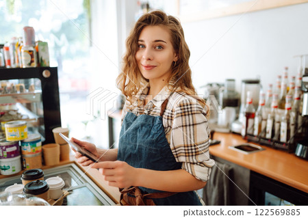 Portrait of a friendly female barista holding a tablet computer and smiling. Takeaway concept 122569885