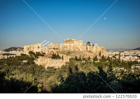 The acropolis in Athens is beautifully surrounded by trees and day moon. Greece The acropolis in Athens is beautifully surrounded by trees and day moon. Greece 122570020