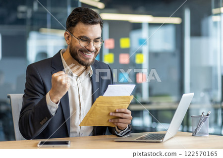 Successful businessman at workplace inside office with letter in hands. Man celebrates successful achievement results, received email notification, reads good news message. 122570165