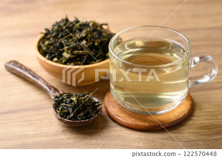 Hot green tea in cup glass and dried tea leaves in bowl with spoon on wooden background Hot green tea in cup glass and dried tea leaves in bowl with spoon on wooden background 122570448