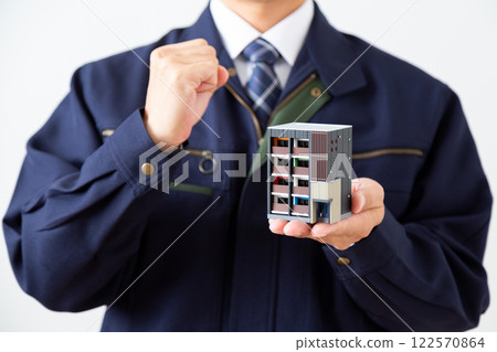 一名身穿深藍色工作服的中年男子手裡拿著一棟公寓大樓的模型,揮舞著拳頭 一名身穿深藍色工作服的中年男子手裡拿著一棟公寓大樓的模型,揮舞著拳頭 122570864