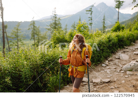 Traveler with hiking poles, bright backpack enjoys mountain scenery along hiking trail. Wanderlust. 122570945