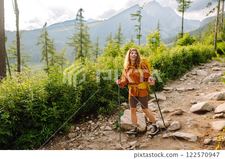 Traveler with hiking poles, bright backpack enjoys mountain scenery along hiking trail. Wanderlust. 122570947