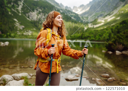 Travel Slovakia, Europe. Tourist with a yellow backpack stands against the backdrop of alpine lake. Travel Slovakia, Europe. Tourist with a yellow backpack stands against the backdrop of alpine lake. 122571010
