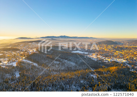 A peaceful winter evening unfolds over Jablonec nad Nisou with the snow-covered hills of the Jested Ridge in the background. The serene landscape captures the beauty of Czechia in winter. 122571040