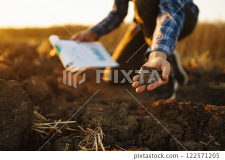 Farm owner checks quality of soil with his hands with tablet and checks fertility before sowing. Farm owner checks quality of soil with his hands with tablet and checks fertility before sowing. 122571205