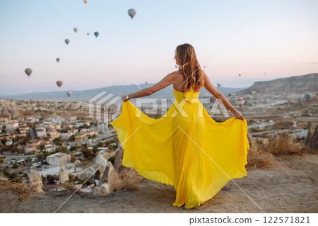 Woman stands on mountain with flying air balloons on background. Tourist Turkish region Cappadocia. 122571821