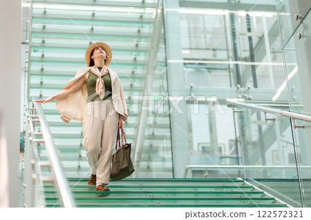 Wide shot of a Caucasian pretty young elegant woman in a straw hat looking up. In the background is a modern business building. Copy space 122572321